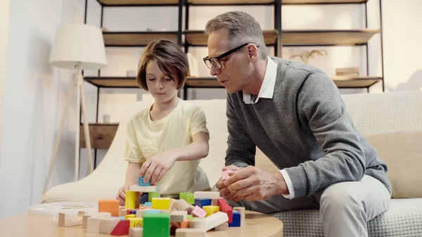 Abuelo de mediana edad jugando bloques de construcción con nieto preadolescente - foto de stock