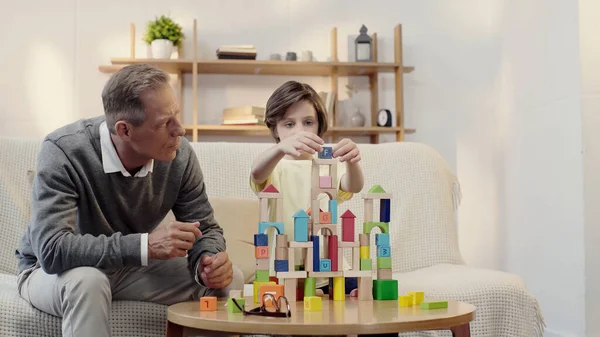 Middle aged grandfather playing building blocks with preteen kid — Stock Photo