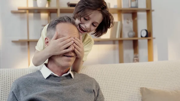 Preteen boy covering eyes of grandfather and playing guess who game — Photo de stock