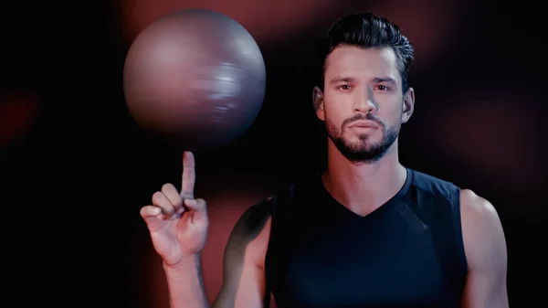 Serious young sportsman spinning blurred basketball on finger on black — Stock Photo