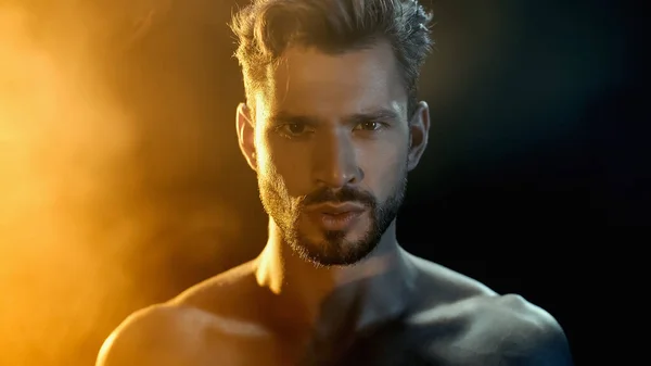 Portrait of muscular sportsman looking at camera near smoke on black with yellow lighting — Photo de stock