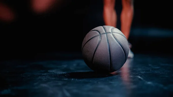 Visão parcial do esportista desfocado em pé perto de basquete no fundo escuro — Fotografia de Stock