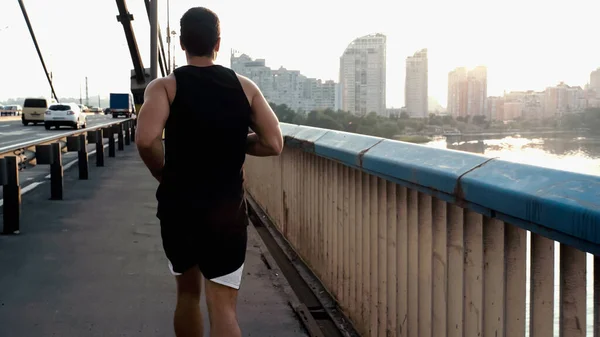 Back view of athletic mixed race man running on city bridge over river — Stock Photo
