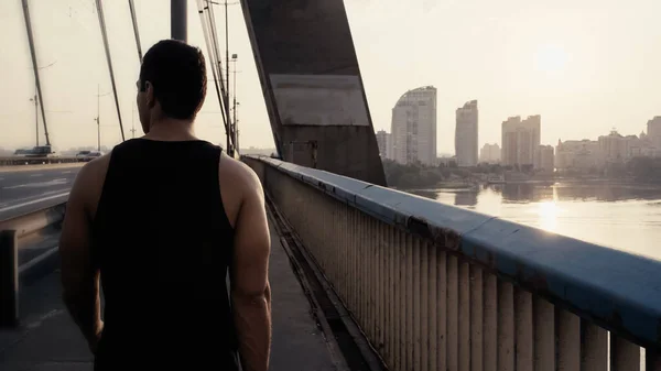 Vista posteriore dello sportivo mista uomo corsa a piedi sul ponte della città — Foto stock