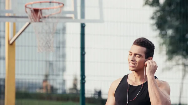 Joven deportista bi-racial con los ojos cerrados ajustando auriculares al aire libre - foto de stock