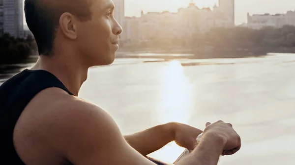 Young and sportive b-racial man standing on bridge over river at dawn — Stock Photo