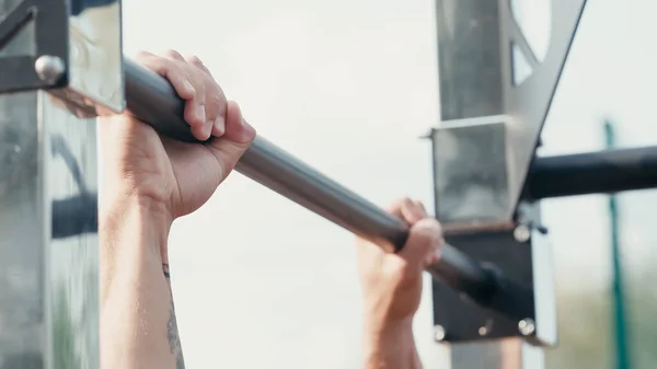 Cropped view of sportsman working out on horizontal bar outdoors — Stock Photo