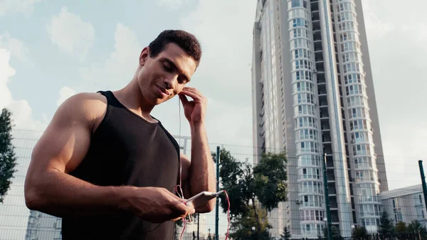 Sonriente deportista bi-racial con smartphone insertando auriculares al aire libre - foto de stock