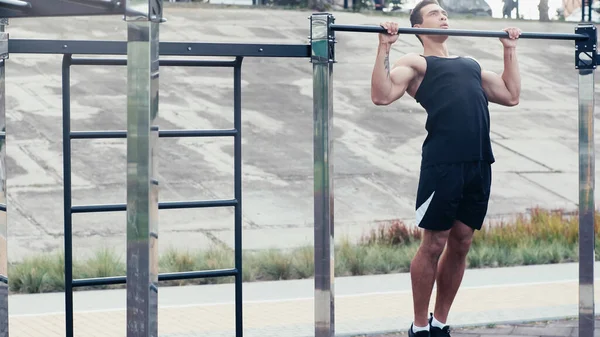 Bi-racial man in sportswear exercising on horizontal bar outdoors — Stock Photo