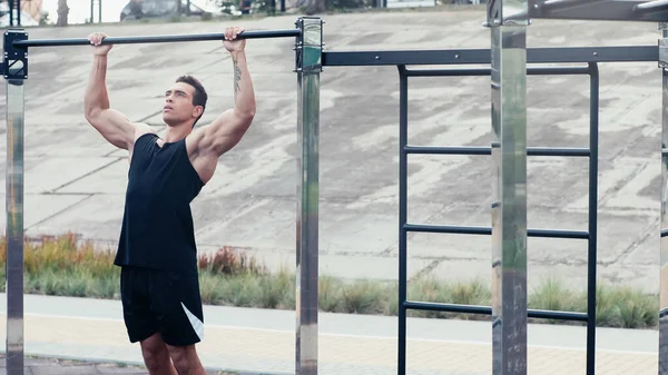 Tätowierter Mann in Sportbekleidung beim Training am Reck im Outdoor-Fitnessstudio — Stockfoto