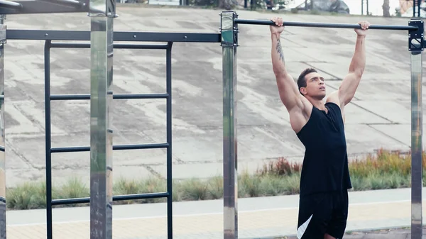 Tattooed mixed race sportsman training on horizontal bar at outdoor gym — Stock Photo