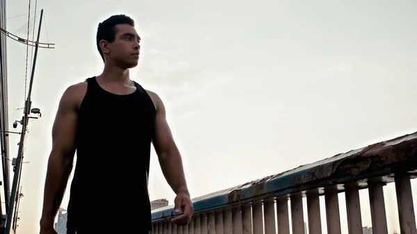 Low angle view of athletic bi-racial man walking on city bridge — Stock Photo