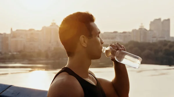 Athletic mixed race man drinking water over river in city — Stock Photo