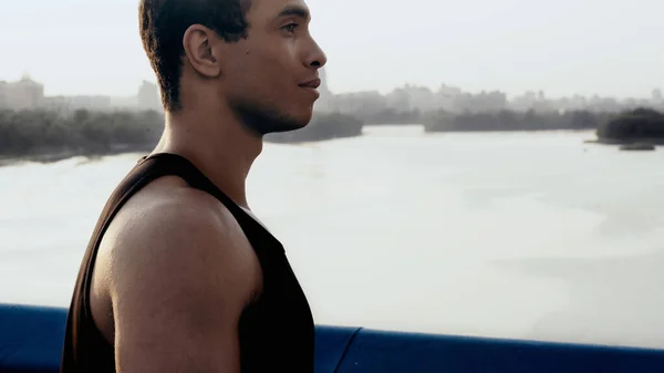Vista lateral do jovem bi-racial homem na cidade ponte sobre o rio — Fotografia de Stock