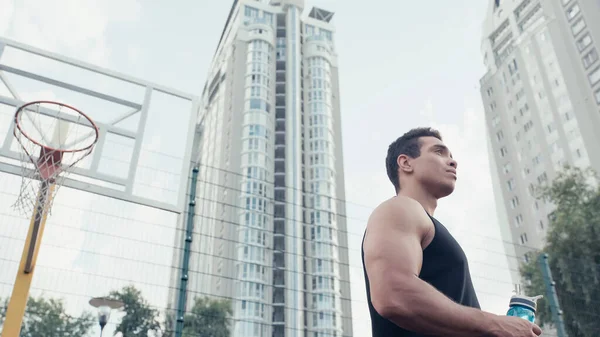 Low angle view of mixed race sportsman with sports bottle looking away outdoors — Stock Photo