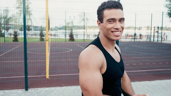 Cheerful bi-racial sportsman looking at camera near outdoor gym — Stock Photo