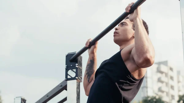 Татуированный бирасовый спортсмен, работающий на горизонтальной полосе на открытом воздухе — стоковое фото