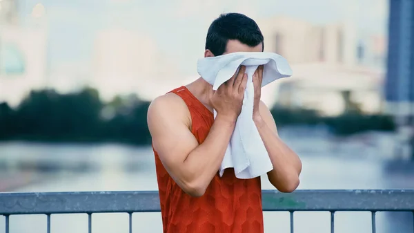 Young sportsman wiping face with towel while standing on bridge — Stock Photo