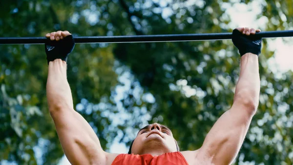 Low angle view of strong sportsman doing pull ups on horizontal bar outside — Stock Photo