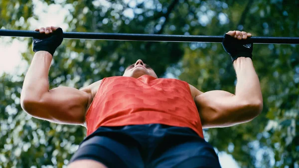 Bottom view of muscular sportsman doing pull ups on horizontal bar outside — Stock Photo