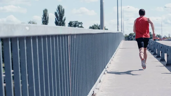 Vista trasera del joven deportista corriendo en puente urbano en verano - foto de stock