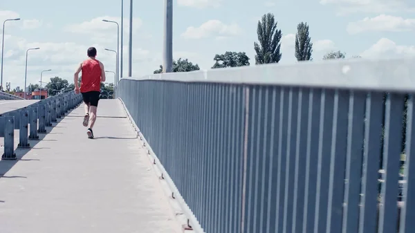 Rückansicht junger Sportler läuft im Sommer über Brücke — Stockfoto