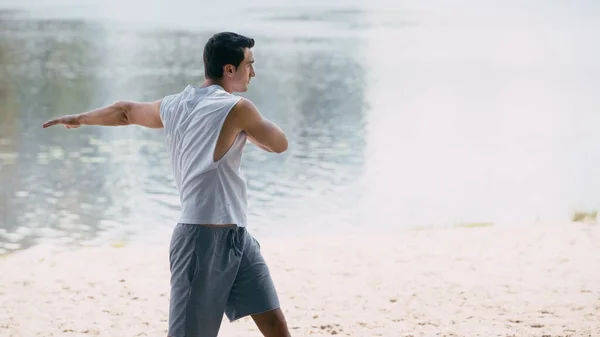 Side view of athletic young sportsman warming up near river — Stock Photo