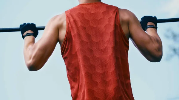 Cropped view of young sportsman doing pull ups on horizontal bar outside — Stock Photo