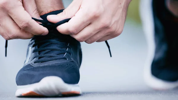 Recortado vista de deportista atando cordones en zapatilla de deporte - foto de stock