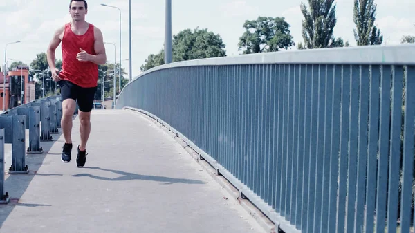 Jeune joggeuse en débardeur et short courant sur le pont — Photo de stock