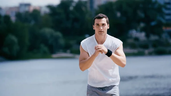 Joven deportista en camiseta sin mangas haciendo ejercicio cerca del río - foto de stock