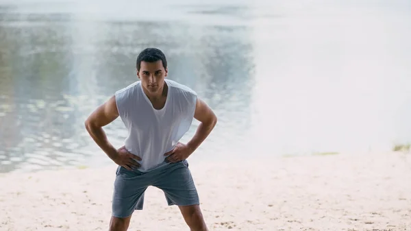 Young sportsman in tank top working out with hands on hips near river — Stock Photo