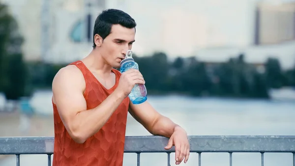Müder Sportler steht auf Brücke und trinkt Wasser aus Sportflasche — Stockfoto