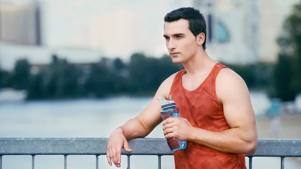 Esportista cansado de pé na ponte com garrafa de esportes — Fotografia de Stock