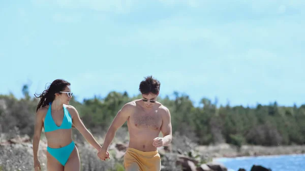 Young couple in sunglasses and swimwear walking on beach — Stock Photo