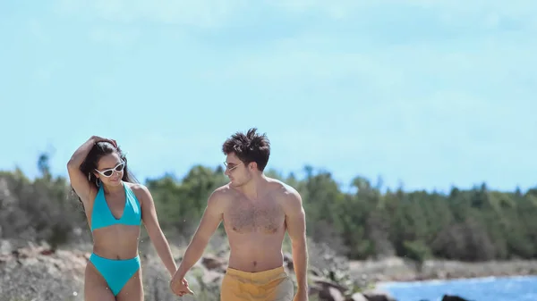 Улыбающаяся женщина в купальнике держит за руку парня на пляже — стоковое фото