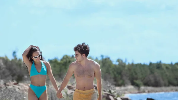 Smiling woman in swimsuit holding hand of boyfriend on beach — Stock Photo