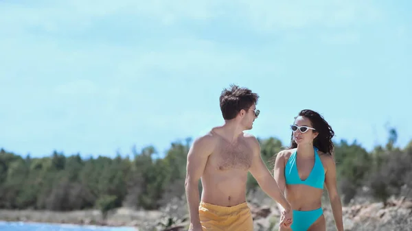 Junger Mann mit Sonnenbrille hält Hand seiner Freundin im Badeanzug am Strand — Stockfoto