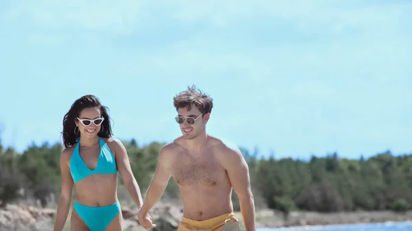 Cheerful couple in swimwear holding hands on beach — Stock Photo