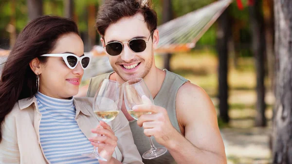 Pareja sonriente en gafas de sol sosteniendo copas de vino en la playa - foto de stock