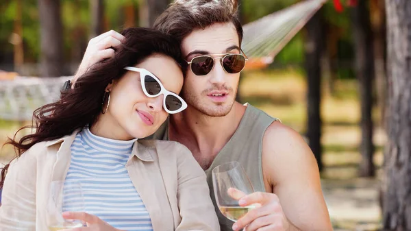 Hombre en gafas de sol sosteniendo el vino y tocando novia en la playa - foto de stock