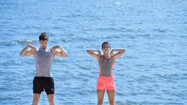 Couple in sportswear training on beach near sea — Stock Photo