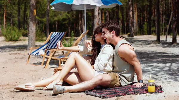 Cheerful man in sunglasses taking selfie with girlfriend on beach — Stock Photo