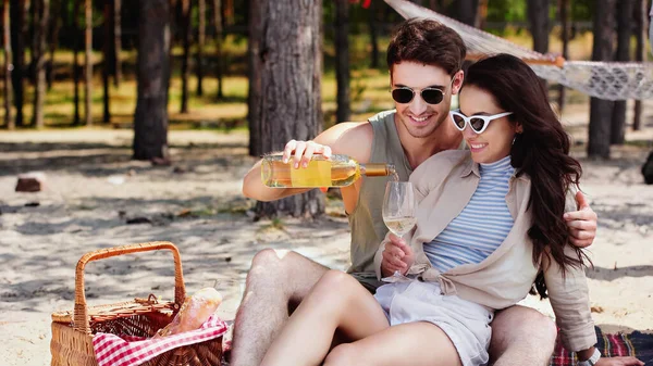 Hombre en gafas de sol verter vino cerca de novia en la playa - foto de stock