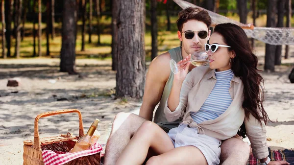 Woman in sunglasses drinking wine near boyfriend on beach — Stock Photo