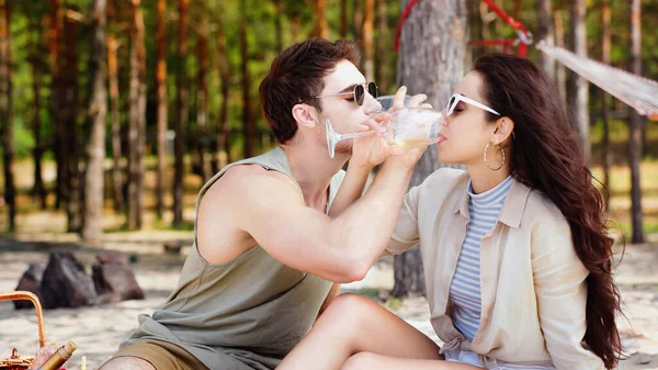 Couple en lunettes de soleil buvant du vin pendant le pique-nique sur la plage — Photo de stock