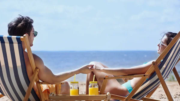 Молода пара в купальнику тримає руки біля апельсинового соку на пляжі — стокове фото