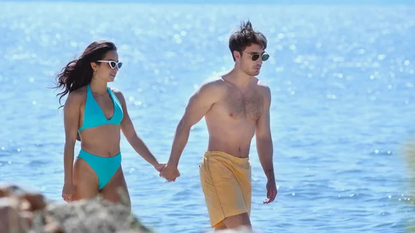 Smiling couple in swimwear holding hands near blurred sea — Stock Photo
