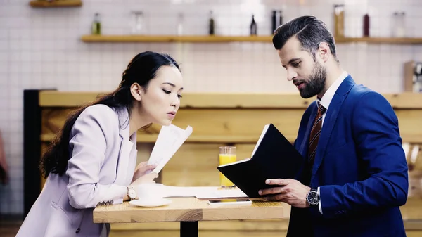 Азиатская бизнесвумен смотрит на ноутбук рядом с бизнесменом в кафе — стоковое фото