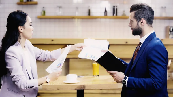 Vista lateral da mulher de negócios asiática mostrando gráficos e gráficos para homem de negócios no café — Fotografia de Stock